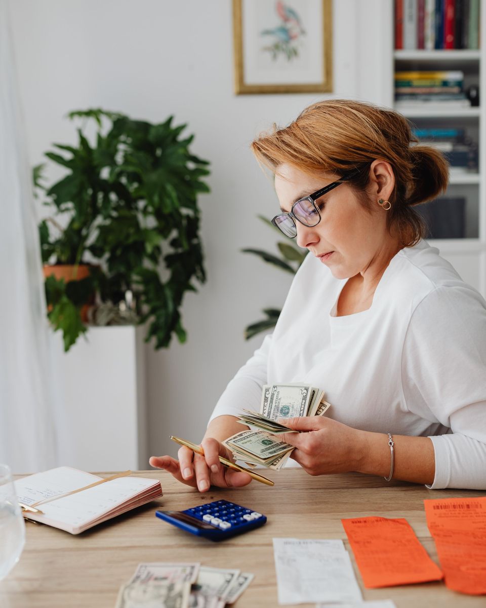 Woman counting cash beside a calculator and notebook while planning payments
